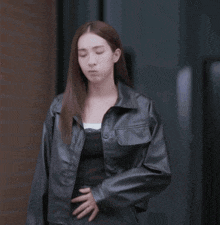 a woman wearing a black leather jacket is standing in front of a building