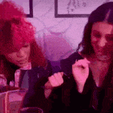 two women are sitting next to each other in a room with purple lights . one of the women has red hair .