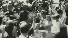 a black and white photo of a crowd of people holding their hands up in the air .