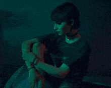 a woman wearing a choker sits in a dark room with green light behind her