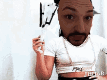 a man with a beard is wearing a white crop top and holding a fan .
