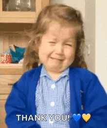 a little girl in a blue sweater is smiling and saying thank you