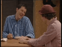 two men are sitting at a table with one wearing a red hat