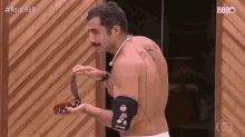 a shirtless man with a mustache is standing in front of a wooden wall holding a belt .