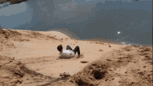 a person is laying on a sand dune near a body of water