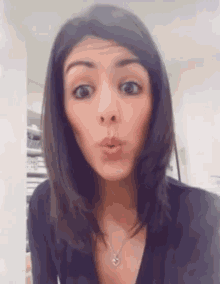 a woman wearing a black shirt and a necklace with a heart on it makes a funny face