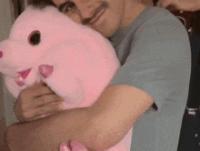 a man in a blue shirt is hugging a large pink stuffed animal