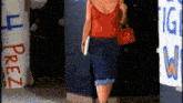 a woman in a red tank top and blue shorts is walking in front of a sign that says free .