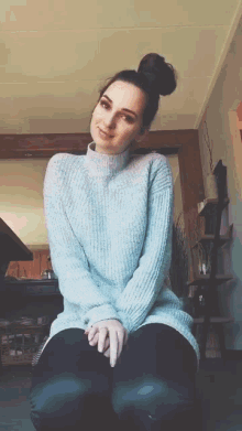 a woman wearing a grey sweater is kneeling down in a living room