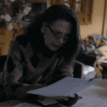 a woman wearing glasses is sitting at a table looking at papers