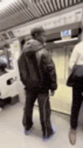 a man in a black jacket is standing in a subway station next to a woman .