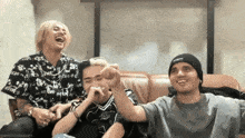 three men are sitting on a couch and one of them is wearing a black hat