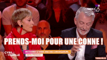a man and a woman are sitting in front of a crowd with the words prends-moi pour une conne on the screen