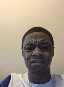 a young man is making a funny face while looking at the camera against a white wall .