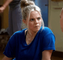 a woman in a blue shirt is sitting on the floor and looking at the camera .