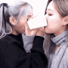 two girls are drinking from the same cup and kissing each other .