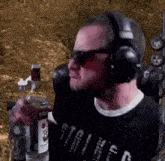 a man wearing headphones and sunglasses is drinking from a glass while holding a bottle of vodka .