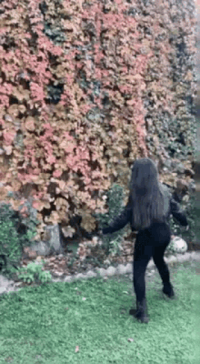 a woman is standing in the grass in front of a bush with leaves changing colors .