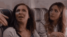 two women are sitting next to each other on a couch on a plane .