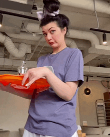 a woman in a blue shirt is holding an orange tray and making a funny face
