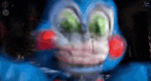 a blue stuffed animal with green eyes and red cheeks is looking at the camera .
