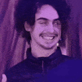 a man with curly hair and a beard is smiling in a purple room .