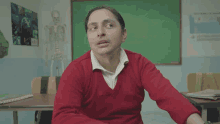 a man in a red sweater sits in front of a green board