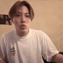 a young man wearing a white t-shirt is making a face .