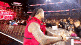 a man in a red vest is standing in front of a crowd at a wrestling event .