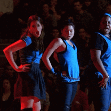 a group of three women in blue shirts are dancing in front of a crowd