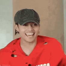a man wearing a red shirt and a black hat is smiling .