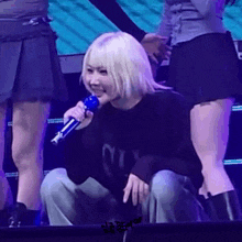 a woman with blonde hair is sitting on the stage holding a microphone and smiling .