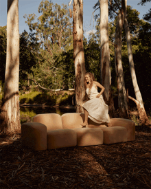 a woman in a white dress is sitting on a couch in the middle of a forest