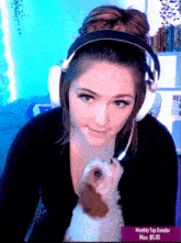 a woman wearing headphones and holding a small brown and white dog with a monthly top donator badge