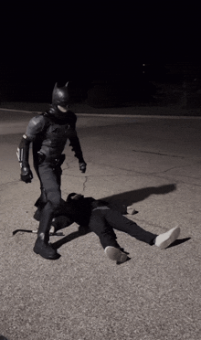 a man in a batman costume is standing over a man laying on the ground