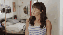 a woman in a striped tank top stands in front of a mirror in a bedroom
