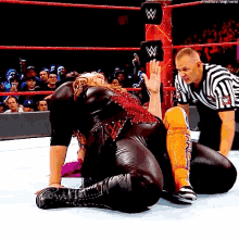 a wrestler is kneeling on the ground in a wrestling ring while a referee watches .