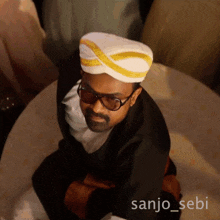 a man wearing sunglasses and a white turban with the name sanjo_sebi on the bottom right