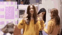 a woman in a yellow sweater is standing next to two other women in front of a sign that says bnk 48 .