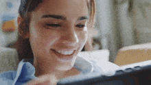 a woman is sitting on a couch looking at a tablet and smiling .