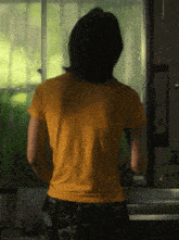 a woman in a yellow shirt is standing in front of a green window