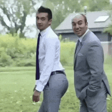 two men in suits and ties are standing next to each other in a grassy field .