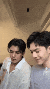 two young men are standing next to each other in a room and smiling .