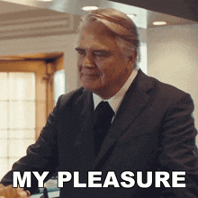 a man in a suit and tie is standing in front of a sign that says " my pleasure "