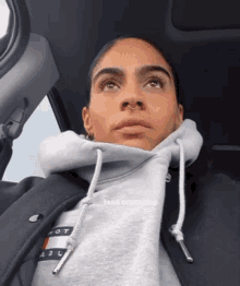 a woman wearing a grey hoodie and a black jacket is sitting in a car looking up .