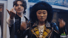 a man and a woman are standing next to each other and the woman is wearing a yellow plaid jacket