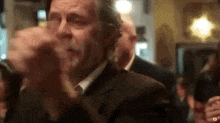 a man in a suit and tie is clapping his hands in front of a crowd .
