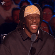 a man wearing a yellow bandana is laughing in front of a microphone