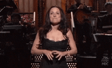 a woman in a black dress is standing in front of a nbc orchestra .