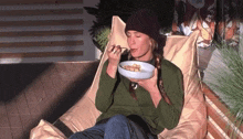 a woman is sitting on a bean bag chair eating food from a bowl .